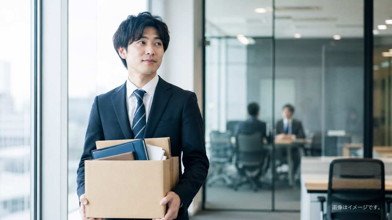 退職を上司に伝えた後、オフィスの窓際で少し不安そうにしながらも前向きな表情を見せる日本人会社員